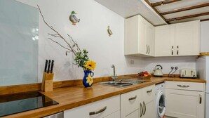 A kitchen with white cabinets, a wooden countertop, a sink, a kettle, a toaster, and a washing machine. - 3 Bed in Ilfracombe (oc-57795) (Ilfracombe)