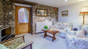 A cozy living room with a stone wall, a wooden door, a sofa, a table with a plant, and a lamp. - 2 Bed in Sedbergh (oc-57641) (Dent)