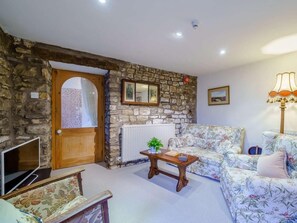 Ein gemütliches Wohnzimmer mit Steinwand, Holztür, einer Couch, einem Tisch mit Pflanze und einer Lampe.