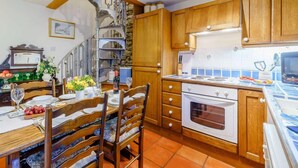 A kitchen with wooden cabinets, a stove, and a dining area with a table set for four. - 2 Bed in Sedbergh (oc-57641) (Dent)
