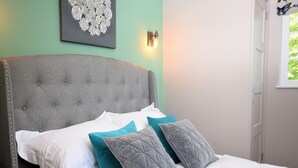 Ein Bett mit einer karossierten Kopfteil, weißen und türkisfarbenen Kissen sowie einer wandmontierten Lampe.