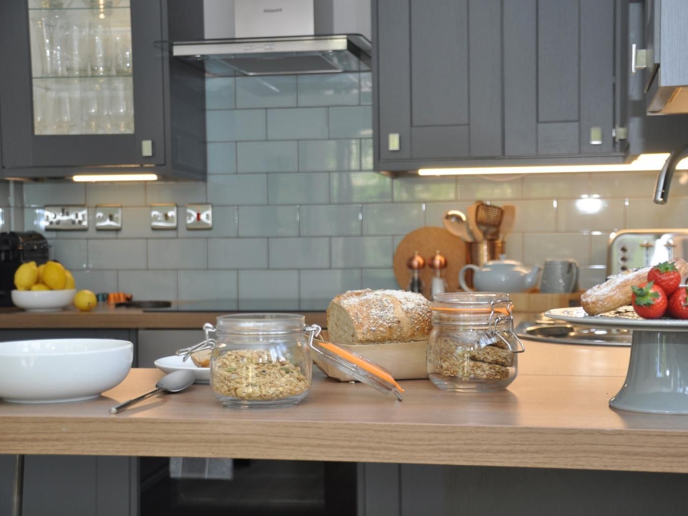 A kitchen with a wooden countertop, jars of food, a loaf of bread, and a bowl of lemons.