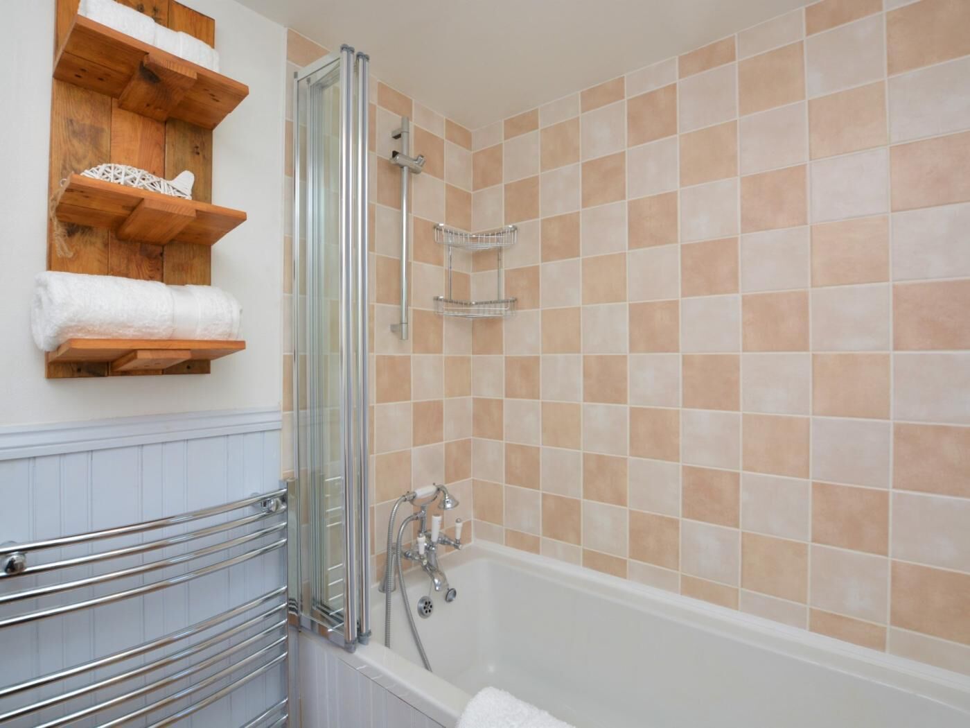 A bathroom with a bathtub, a glass-enclosed shower, and wooden shelves with towels.