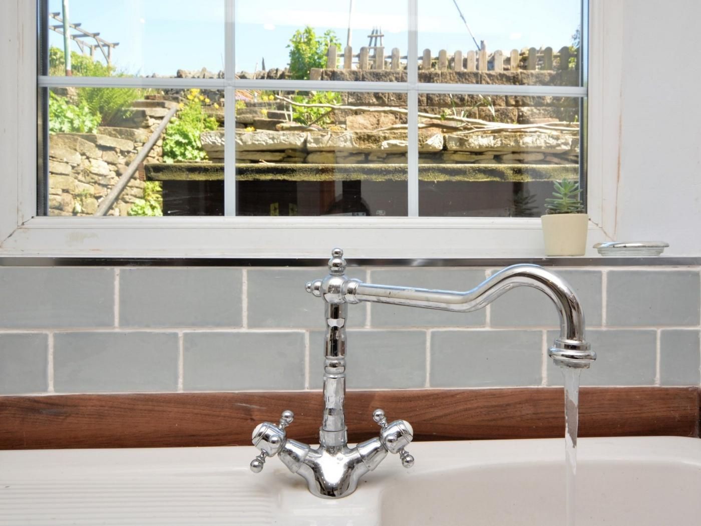 Ein Badezimmer mit einem weißen Waschbecken, einem chromfarbenen Wasserhahn und einem Fenster mit Blick auf Steinwände und Grünpflanzen.