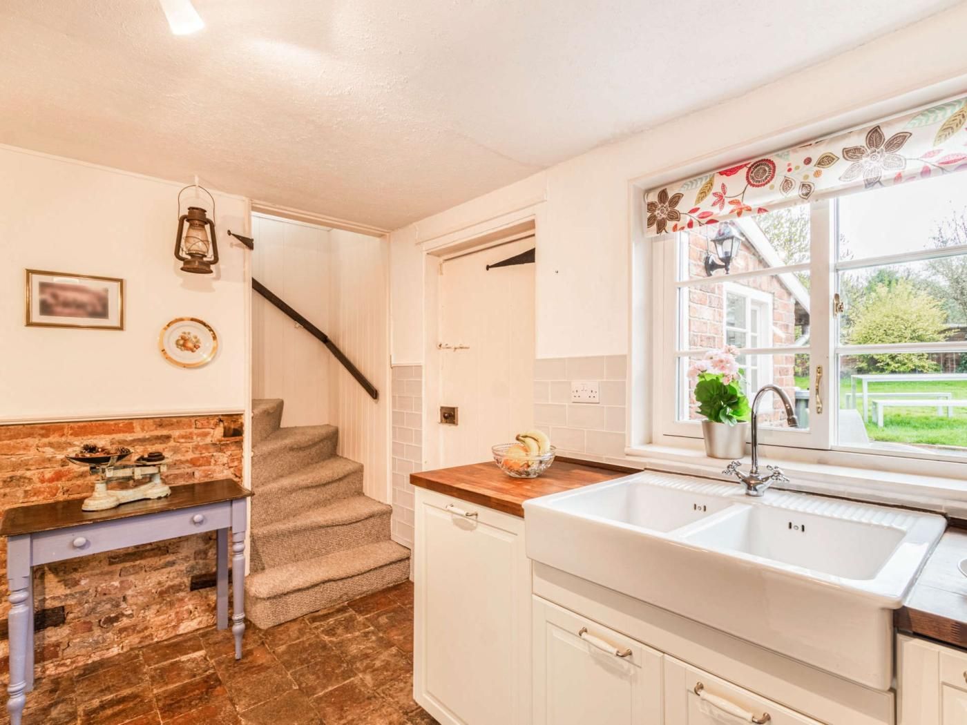 Una cocina con un lavabo blanco, encimera de madera, una escalera y vistas al exterior.