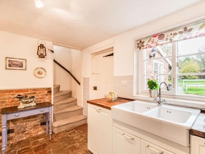 Una cocina con un lavabo blanco, encimera de madera, una escalera y vistas al exterior.
