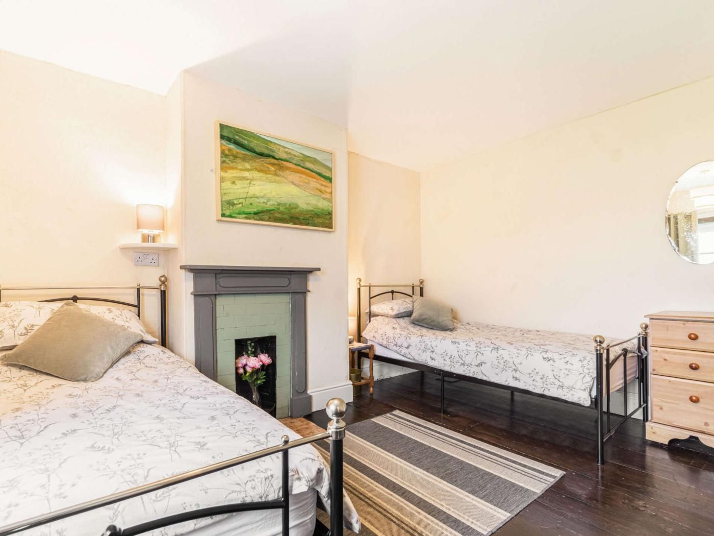 Une chambre avec deux lits, une cheminée, un tableau et une commode.