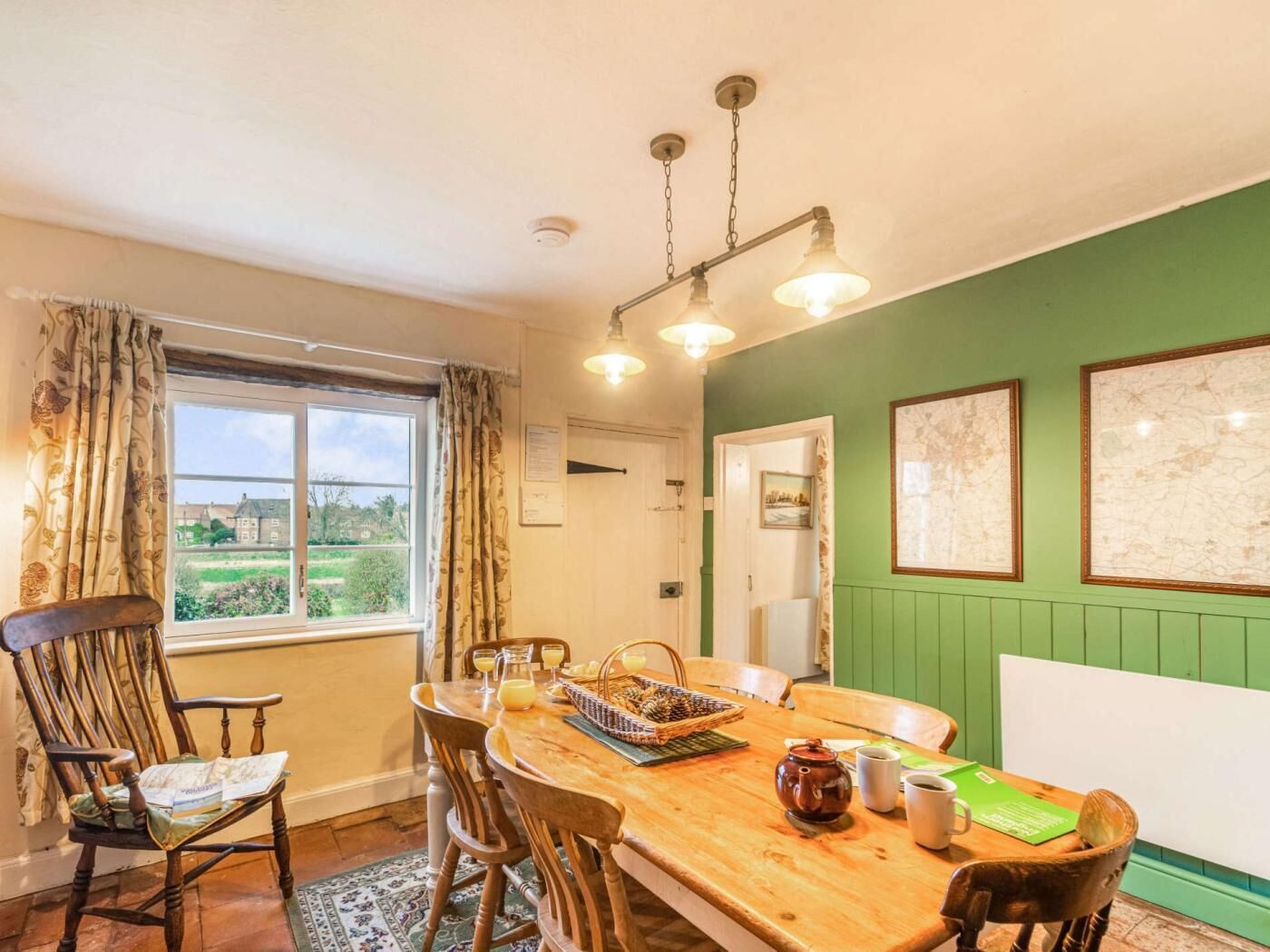 Un coin repas avec une table en bois, des chaises, un lustre et une vue par la fenêtre.