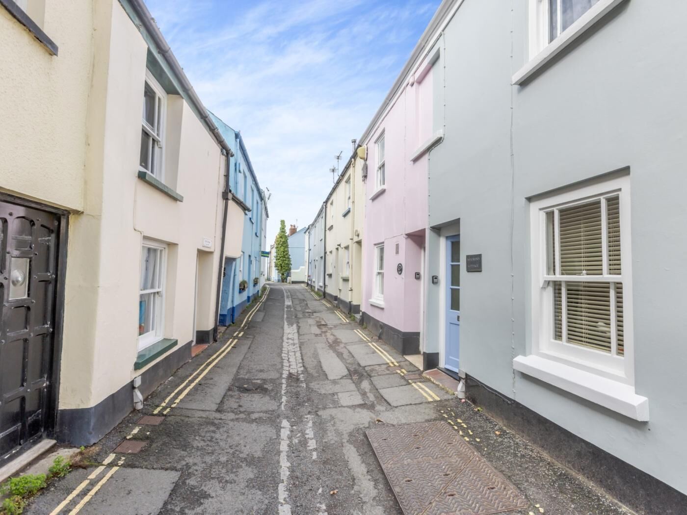 A narrow street with terraced houses, a clear sky, and a visible tree.