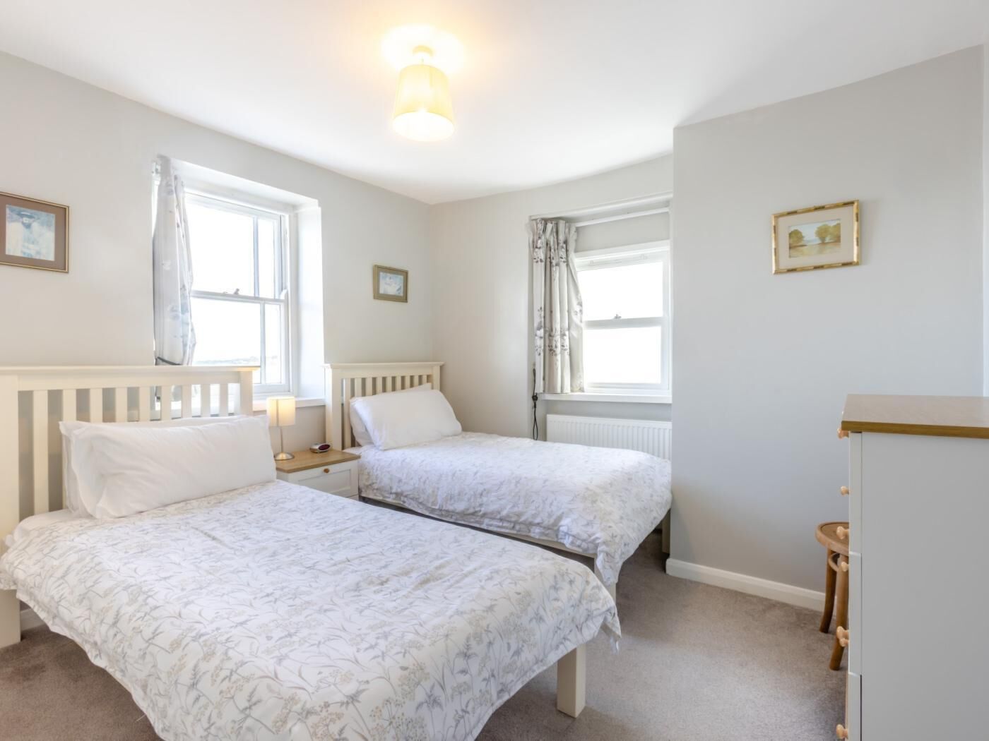 Une chambre avec deux lits, une table de chevet, une commode et une fenêtre avec des rideaux.