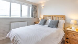 Ein Schlafzimmer mit einem großen Bett, einem Fenster mit Vorhängen, einem Nachttisch mit Lampe und einem Beistelltisch mit Tasse und Gläsern.