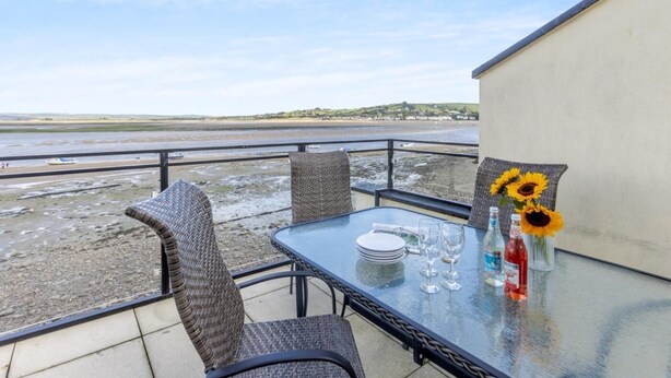 Ein Balkon mit Glastisch, Korbstühlen und Blick auf den Strand.