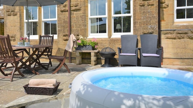 Une terrasse dotée d’un jacuzzi, de meubles d’extérieur et d’un mur en pierre.