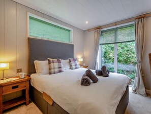 A hotel room with a large bed, a bedside table, a lamp, and a window with curtains. - 2 Bed in Conwy (oc-60292) (Ty'n-y-groes)