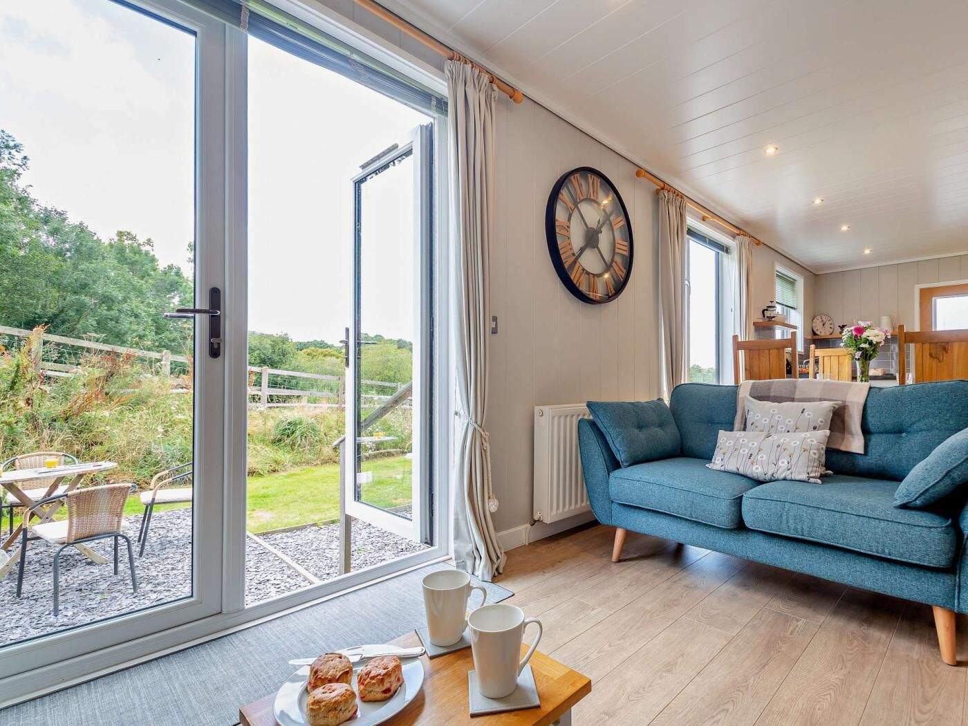 A living room with a blue sofa, a large wall clock, and a view of the outdoors through glass doors.