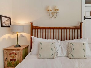 A bed with white linens, two pillows with leaf patterns, a wooden headboard, a nightstand with a lamp, and wall-mounted sconces. - 3 Bed in Bideford (oc-60643) (Buck's Mills)