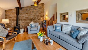 A cozy living room with a stone wall, a fireplace, a sofa, a coffee table, and a wooden chair. - 2 Bed in Morpeth (oc-61267) (Rothbury)