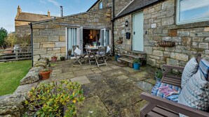A stone building with a patio area, a table with chairs, and a bench. - 2 Bed in Morpeth (oc-61267) (Rothbury)