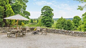 Eine Terrasse mit Holzmöbeln, einer Steinwand und Blick auf eine grüne Landschaft.