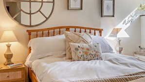 Ein Schlafzimmer mit einem hölzernen Kopfende, einem runden Spiegel und zwei gerahmten Pflanzenbildern an der Wand.
