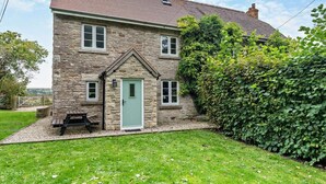 Une maison en pierre avec une porte verte, un petit porche et une cour couverte d’herbe.