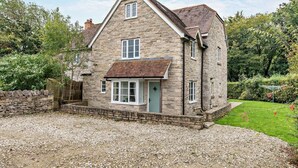 Une maison en pierre avec une allée gravillonnée et une pelouse bien entretenue.