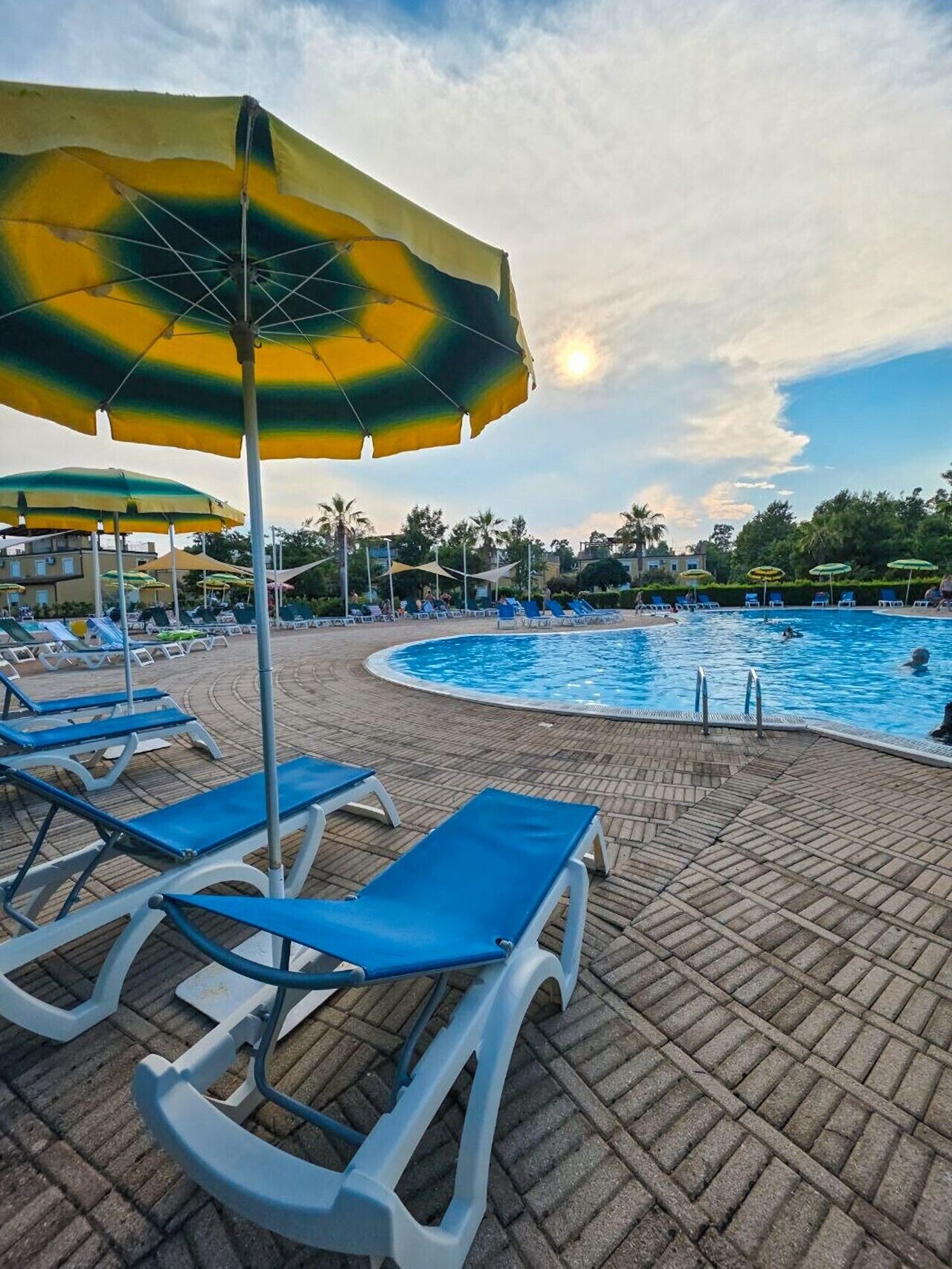 Un espace aménagé au bord de la piscine, avec des chaises longues et des parasols, une piscine et un ciel dégagé.