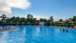 A swimming pool with lounge chairs and umbrellas, surrounded by greenery and buildings. - Casa Onde Chiare - Pizzo Beach Club 16G (Contrada Difesa II)
