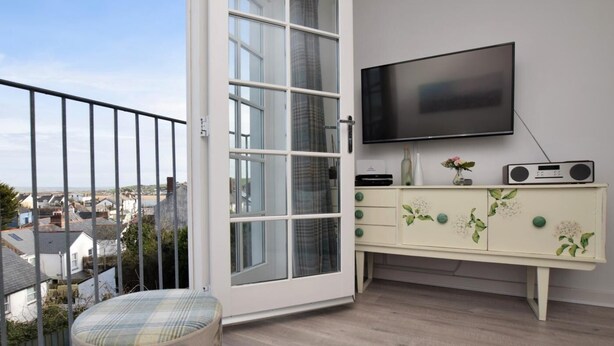 Een balkon met uitzicht op de stad, een aan de muur bevestigde televisie en een kast in vintage-stijl met bloemdecoraties.