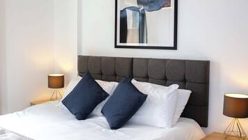 A hotel room with a large bed, two bedside tables, a headboard, a framed artwork, and a lamp.