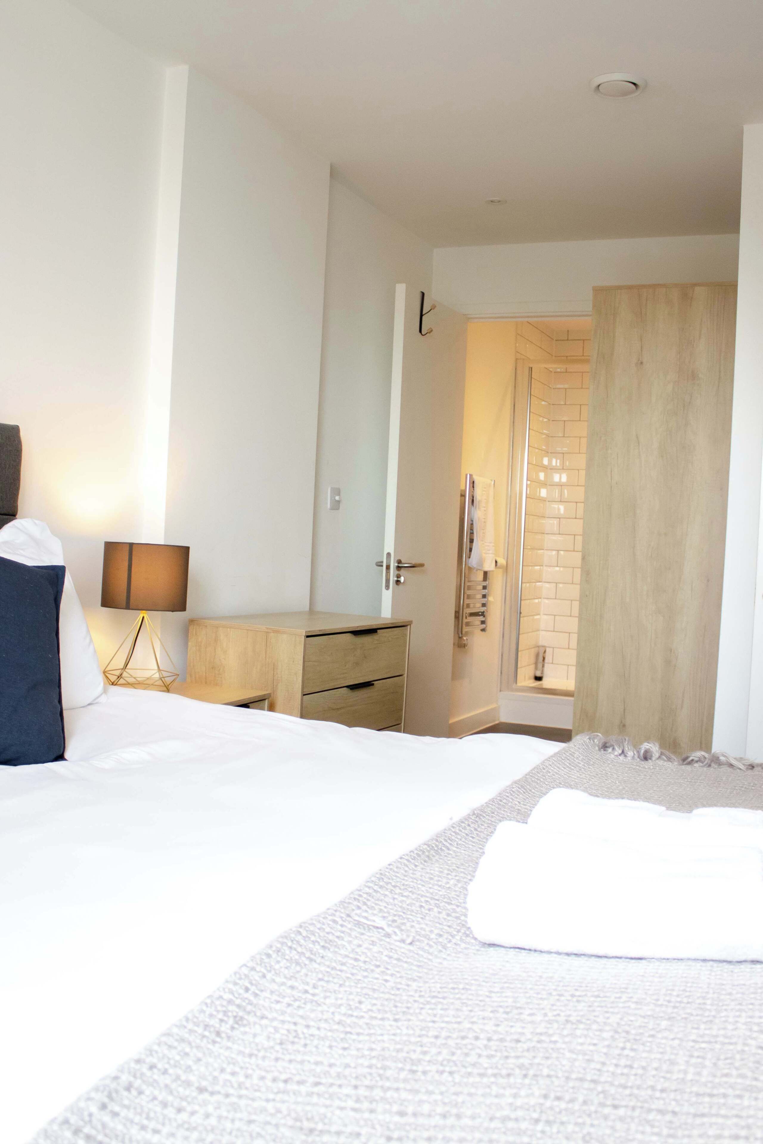 A hotel room with a bed, bedside table, lamp, and a shower area.