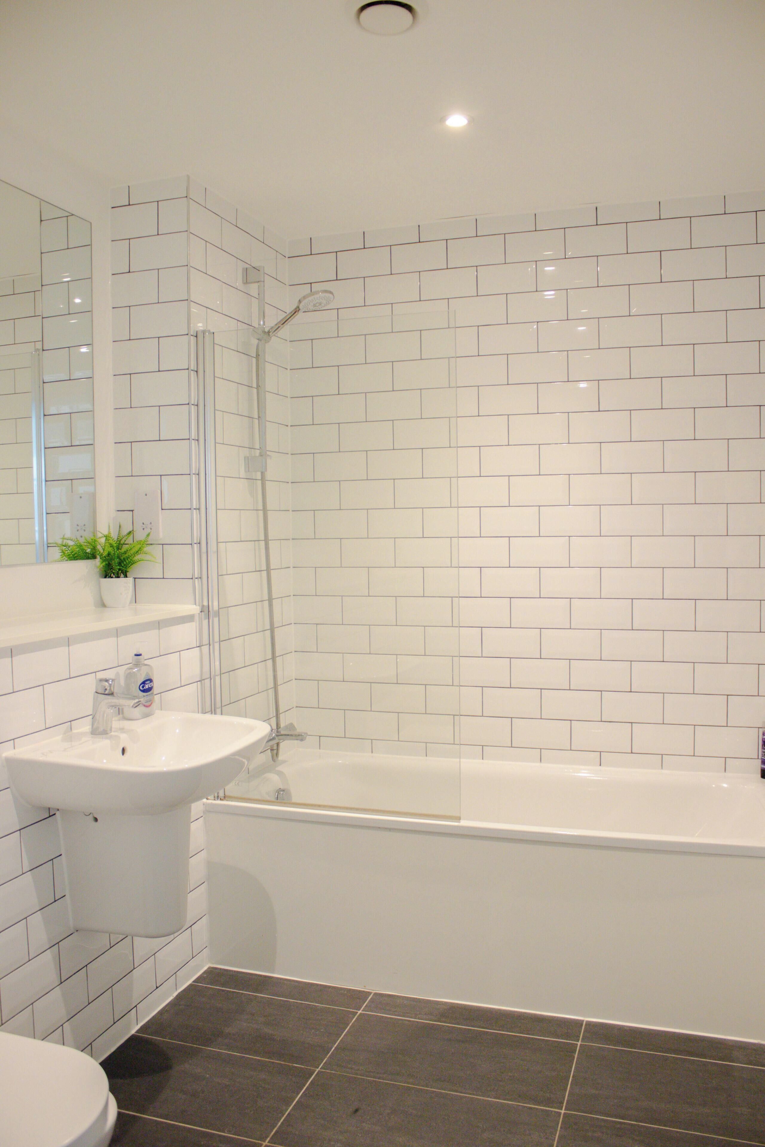 A bathroom with white tiled walls, a white sink, a bathtub, and a shower.