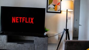 Moderni olohuone, jossa on suuri litteänäyttöinen televisio, jossa näkyy Netflix, lattiavalaisin ja seinällä oleva kehystetty abstrakti taideteos.