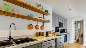 Una cucina moderna con lavello, lavatrice ed scaffali in legno pieni di utensili da cucina.