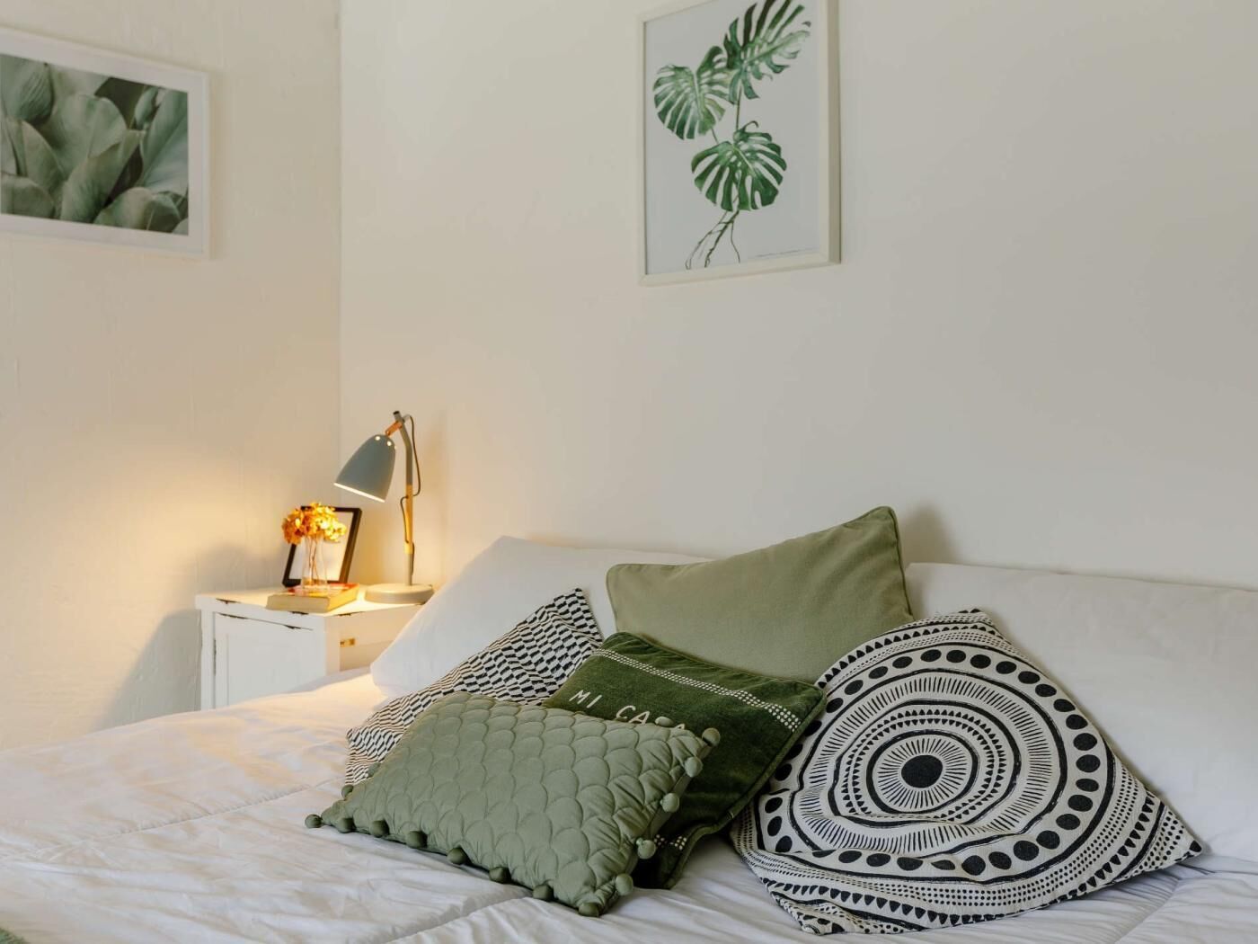 Un lit bien fait, avec des oreillers, une lampe de chevet et une plante en pot posée sur la table de chevet.