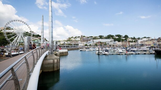 Un marina sul lungomare con barche, una ruota panoramica e un ponte.
