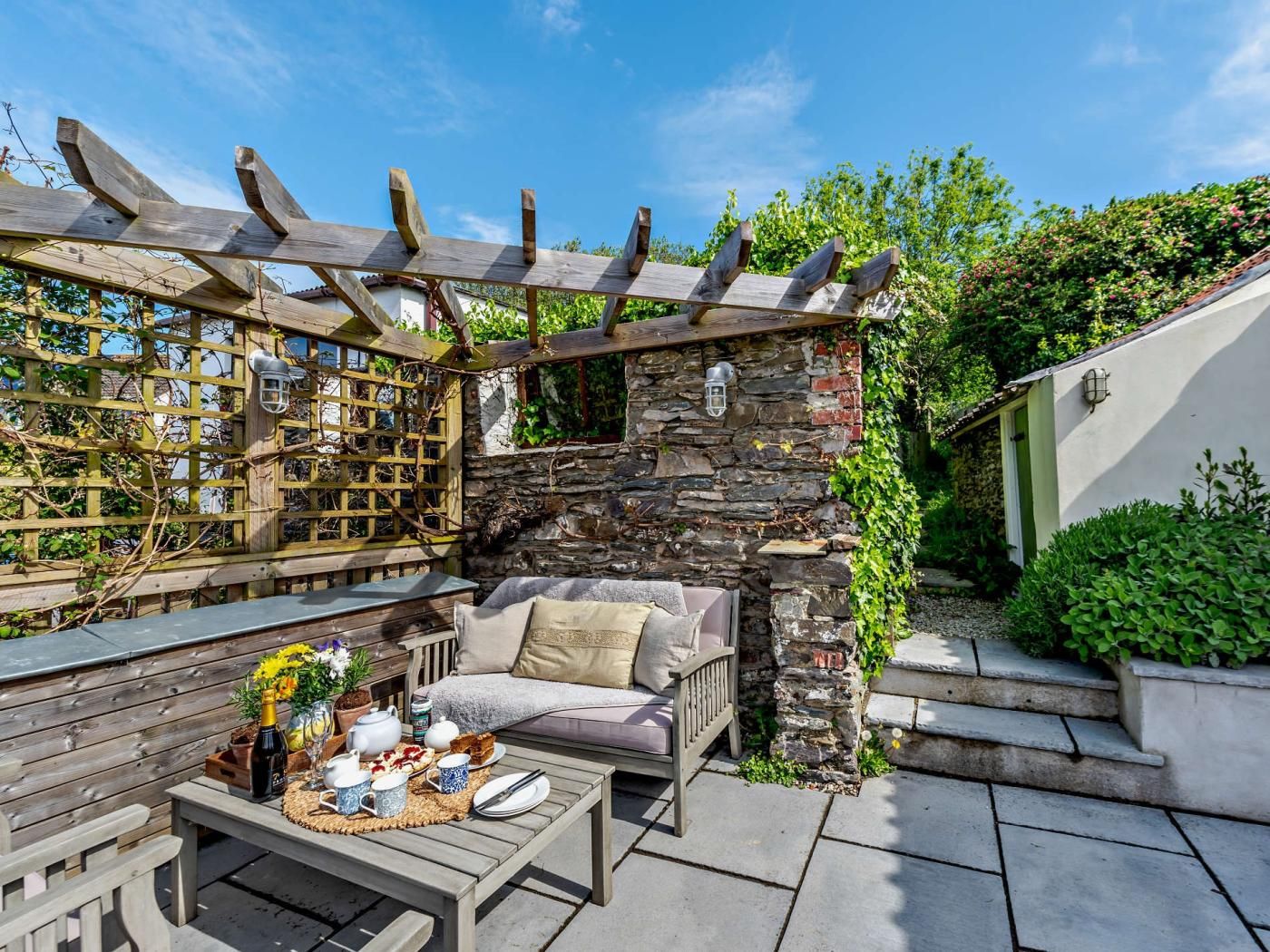 A patio area with a stone wall, wooden pergola, and seating arrangements.