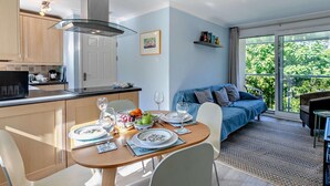 A modern kitchen with a dining area, a sofa, and a view of greenery. - 2 Bed in Newquay (oc-63267) (Newquay)