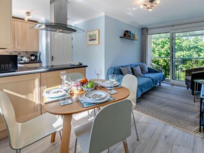 A modern kitchen with a dining area, a sofa, and a view of greenery. - 2 Bed in Newquay (oc-63267) (Newquay)