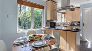 A modern kitchen with wooden cabinets, a central island, and a dining area with a table set for two. - 2 Bed in Newquay (oc-63267) (Newquay)
