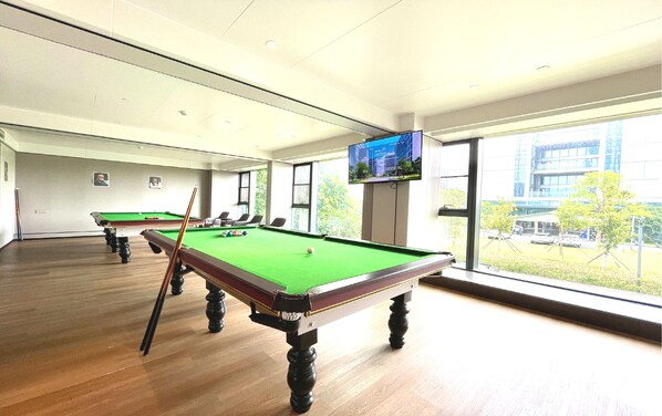 A pool table with a green felt surface, wooden legs, and a pool cue in a room with large windows and a television mounted on the wall. - Grand Skylight Hotel Shenzhen World Exhibition & Convention Center (Shenzhen)