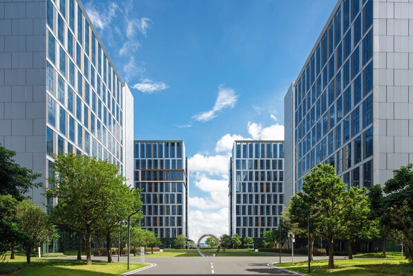 A modern building complex with a central road, surrounded by greenery and trees.
