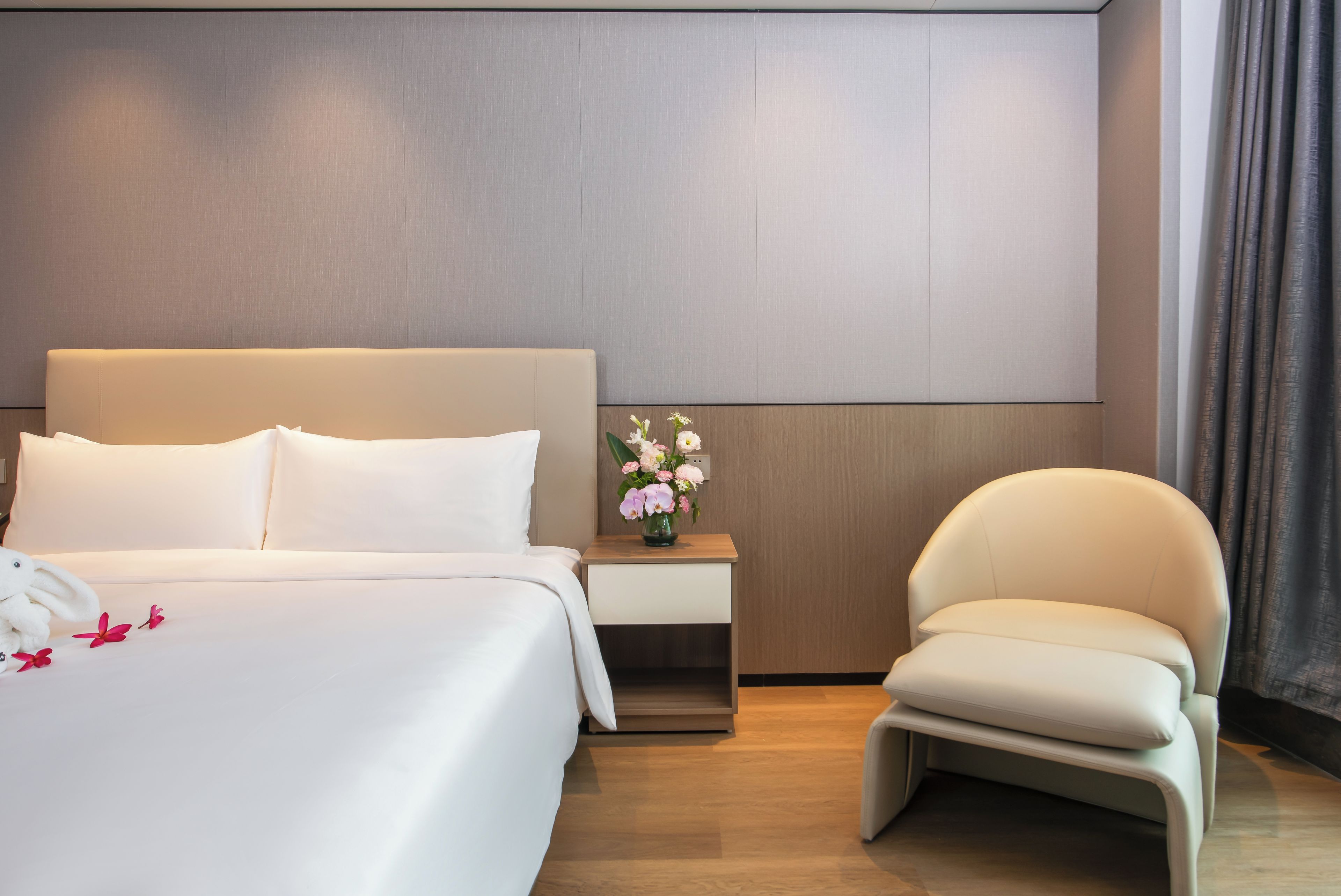 Habitación de hotel con una cama grande, una mesita de noche con un florero, una silla y un panel de pared moderno.