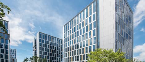Un edificio moderno con fachada de vidrio, rodeado de un césped cuidado y árboles.