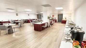 Una amplia sala de conferencias con varias mesas y sillas, equipada con una barra de buffet en un lateral.