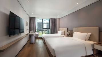 A hotel room with two beds, a flat-screen TV, a small table with a chair, and a window with a city view.