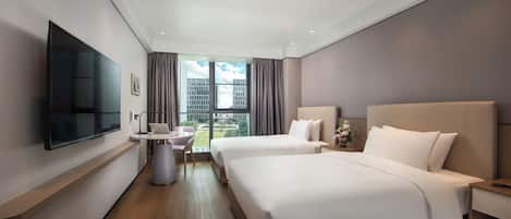 A hotel room with two beds, a flat-screen TV, a small table with a chair, and a window with a city view.