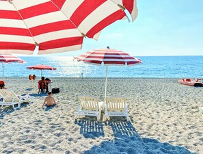 Une plage avec des parasols rayés de blanc et de rouge, des chaises longues blanches et une vue dégagée sur l’océan.