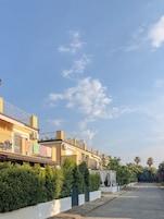 Una calle residencial con casas, un acceso con portones y cielo despejado.