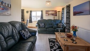 A living room with two leather sofas, a wooden coffee table, and a chandelier. - 3 Bed in Dereham (oc-65903) (Foulsham)